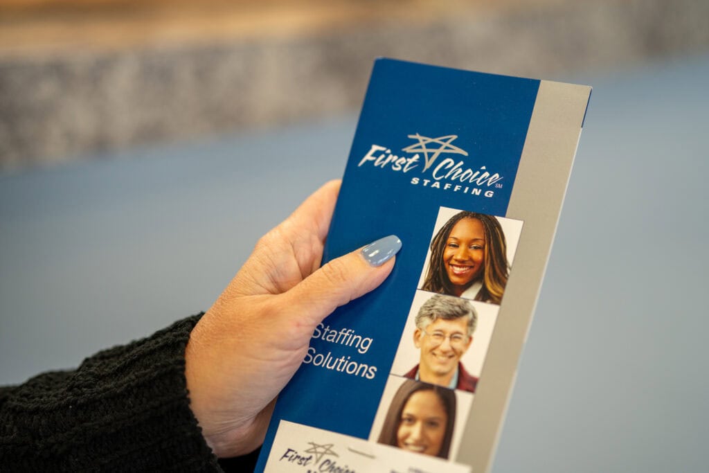 hand holding a brochure for First Choice Staffing with the words Staffing Solutions and photos of 3 individuals