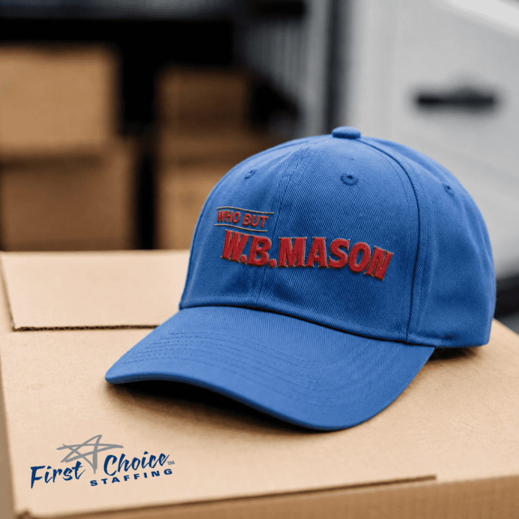 WB Mason Hat sitting on top of a box with the First Choice Staffing star logo. Box is in the foreground of a warehouse